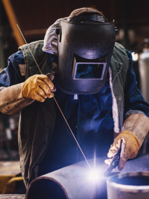 Welder in protective uniform and mask welding metal pipe on the